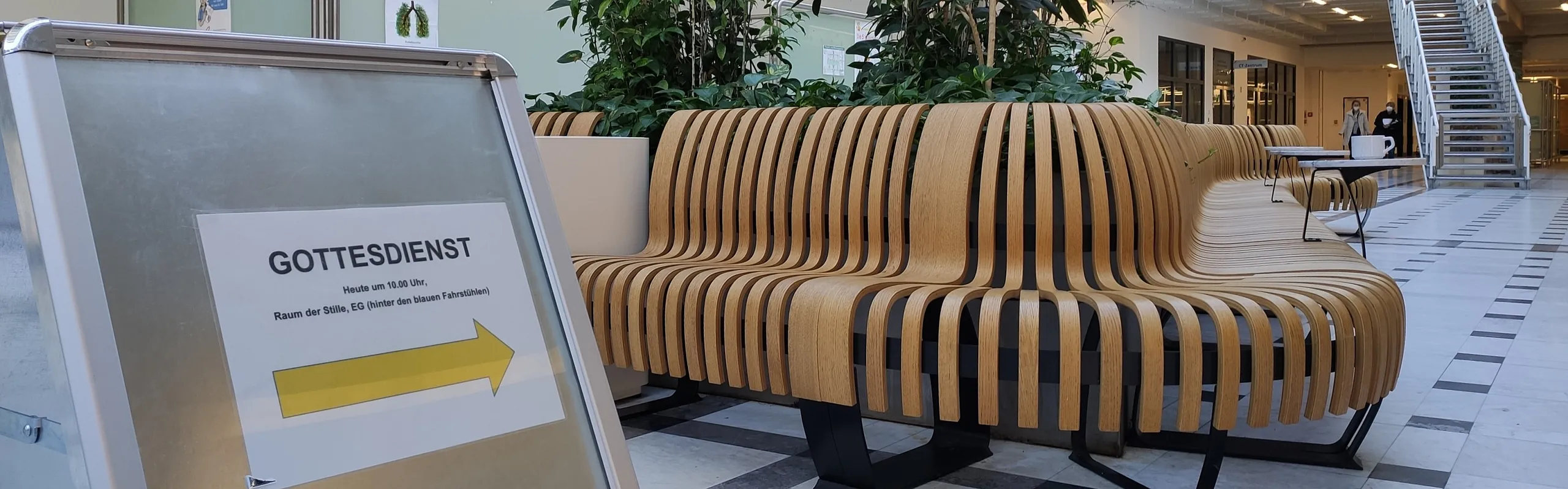 Sitzbank im Krankenhaus-Foyer, daneben Hinweisschild 'Gottesdienst'